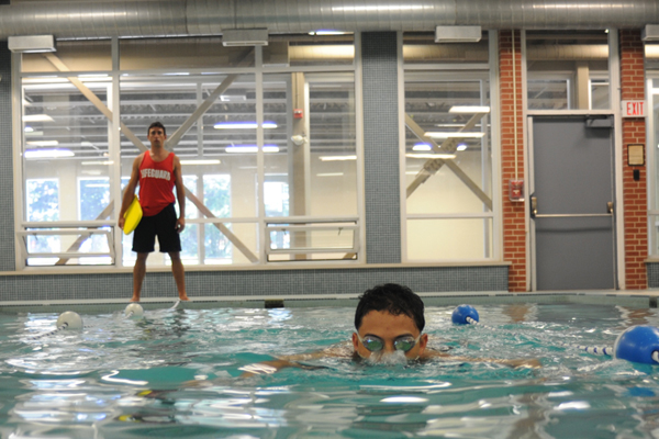 A student swimming in an indoor pool as a lifeguard watches.